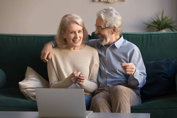 Улыбающиеся пожилые супруги используют ноутбук для просмотра фильма онлайн — стоковое фото