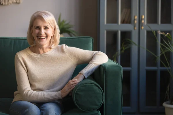 Glückliche Seniorin um die 60 sitzt zu Hause auf Couch — Stockfoto