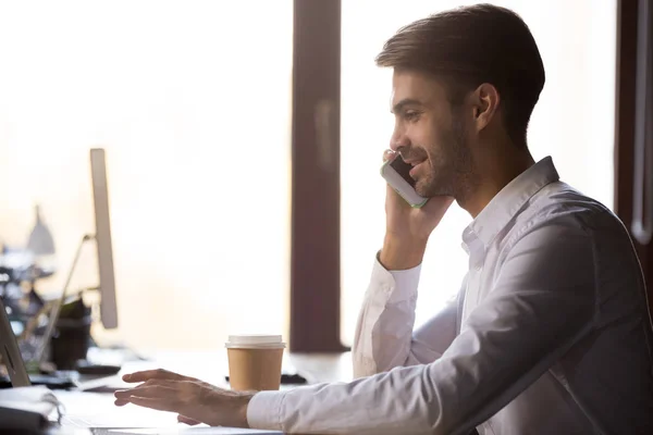 Friendly businessman talking on phone, using laptop, consulting client — Stock Photo, Image