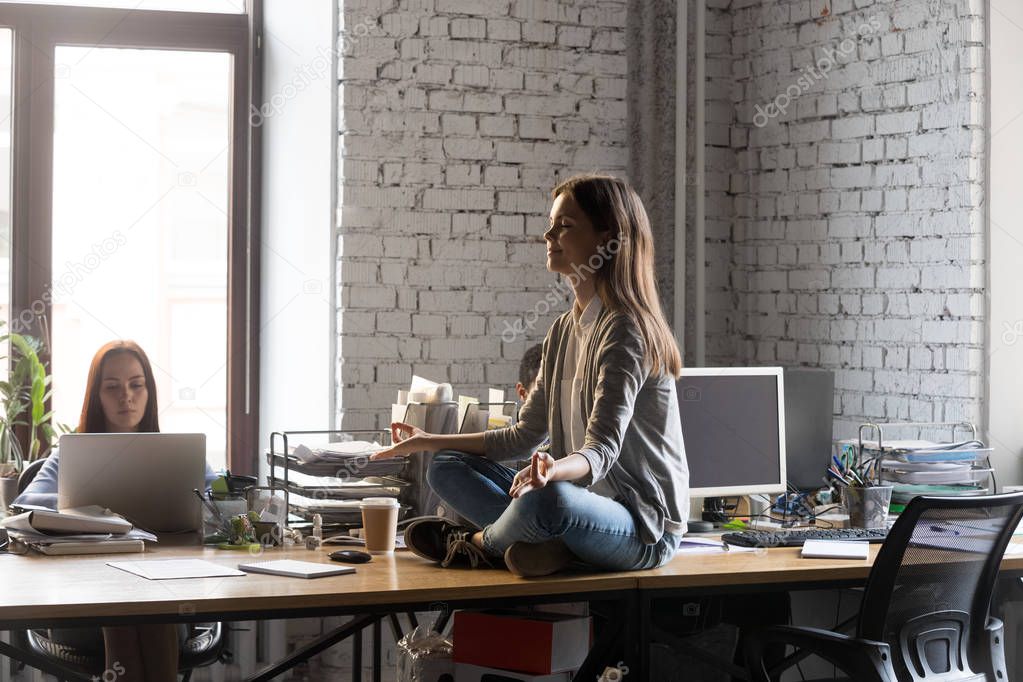 Peaceful businesswoman meditating on office desk, stress relief concept