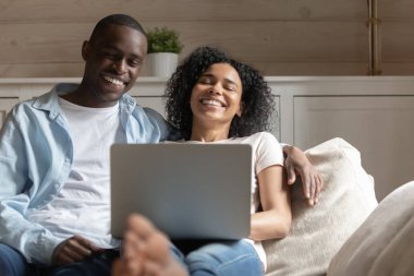 Mutlu biracial çift evde dizüstü bilgisayar kullanarak gülmek dinlenmek