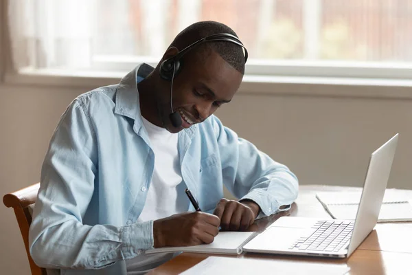 Koncentruje się człowiek biracial w zestawie słuchawkowym piśmie studiowanie na laptopie — Zdjęcie stockowe