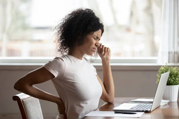 Magoar o trabalho da mulher biracial no laptop sofrem de espasmo na coluna vertebral — Fotografia de Stock