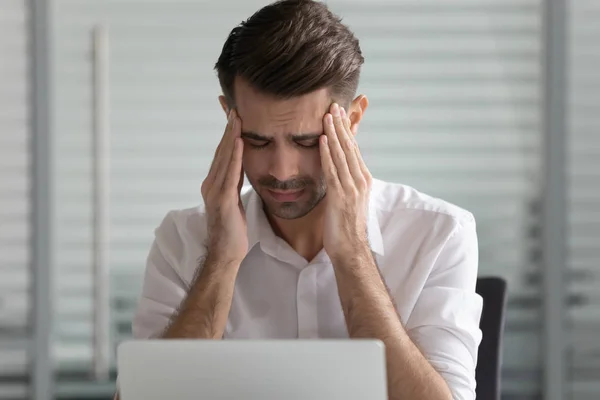 Hoofdschot ongelukkige jonge mannelijke medewerker lijdt aan sterke hoofdpijn. — Stockfoto