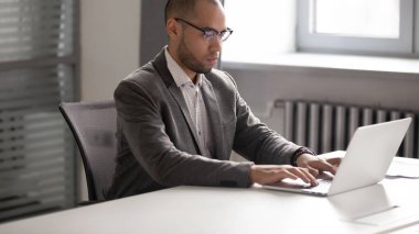 Genç ciddi işadamı yönetim kurulu odasında dizüstü bilgisayar ile çalışıyor.