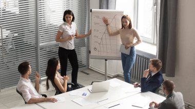 Professional female business trainers giving flip chart presentation to employees.