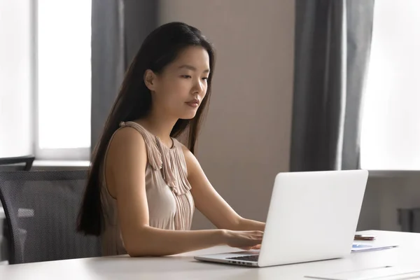 Уверенная азиатская молодая деловая женщина, работающая за компьютером в офисе . — стоковое фото