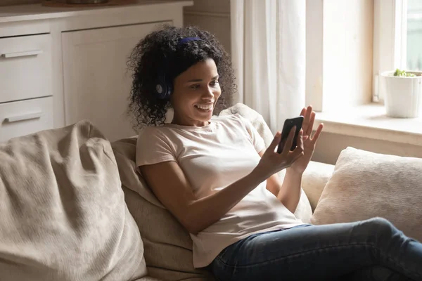 Счастливая расовая женщина в наушниках с помощью смартфона дома — стоковое фото