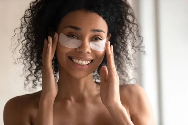 Primer plano de la mujer birracial sonriente aplicar parches debajo de los ojos —  Fotos de Stock