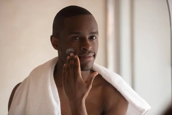 Joven biracial hombre aplicar crema facial después de la ducha — Foto de Stock