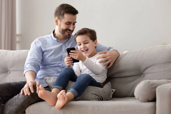 Щасливий тато і син розслабляється на дивані за допомогою телефону — стокове фото