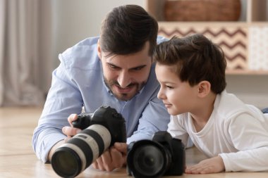 Happy dad and kid son play digital cameras at home clipart