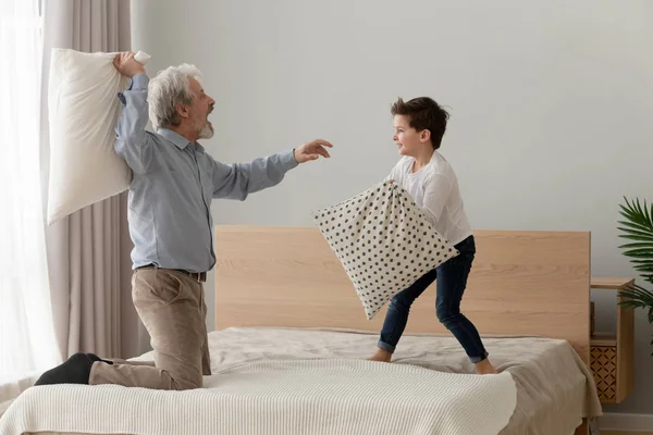 Lucu bahagia kakek dan cucu menikmati perang bantal di tempat tidur — Stok Foto