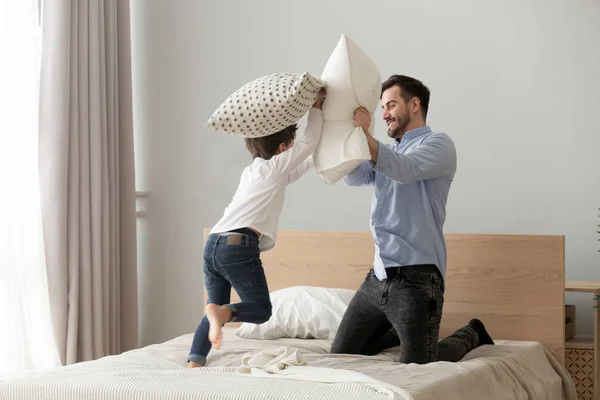 Lindo pequeño hijo jugando almohada lucha en cama con padre —  Fotos de Stock