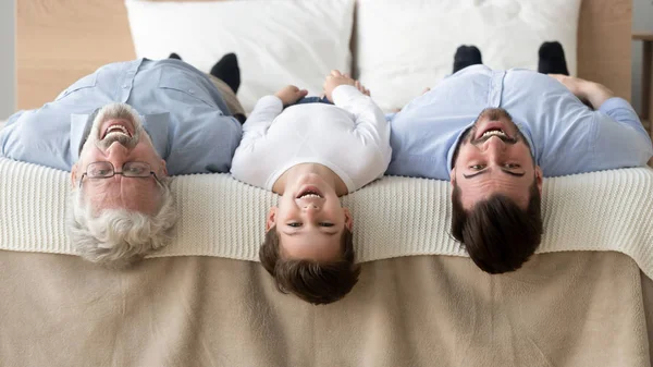 ベッドの上に逆さまに横たわっている幸せな3世代の家族、肖像画 — ストック写真