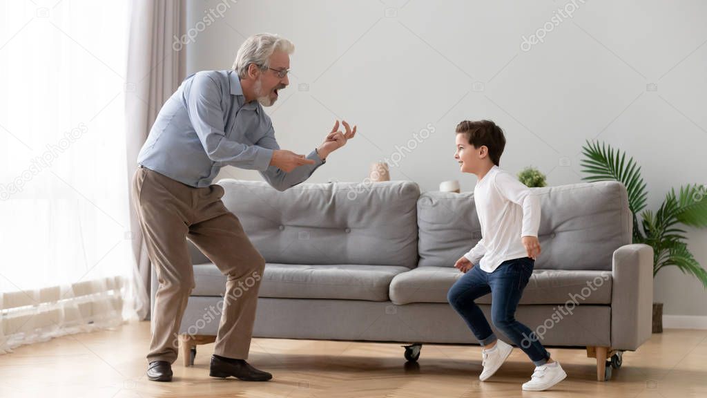 Cute boy grandson dancing with old grandpa in living room
