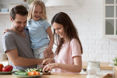 Genç yakışıklı baba kızı tutarak, anne yemek izlerken.