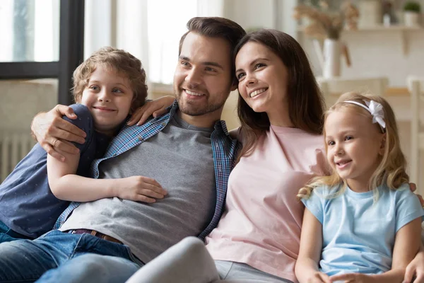 Lyckliga föräldrar sitter med leende barn syskon på bekväm soffa. — Stockfoto