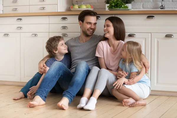 Šťastná rodina čtyř sedí na dřevěné podlaze v kuchyni. — Stock fotografie