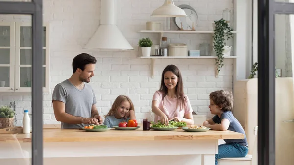 Famille heureuse de quatre personnes préparant ensemble des aliments sains à la cuisine . — Photo