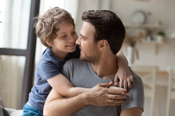 Joyful little preschool boy hugging from back father.