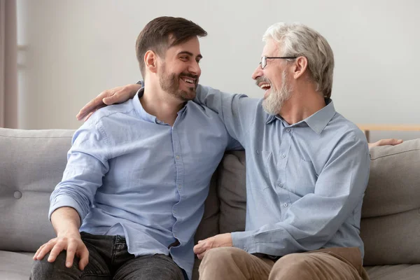 Счастливый старый отец обнимает маленького сына и смеется на диване. — стоковое фото