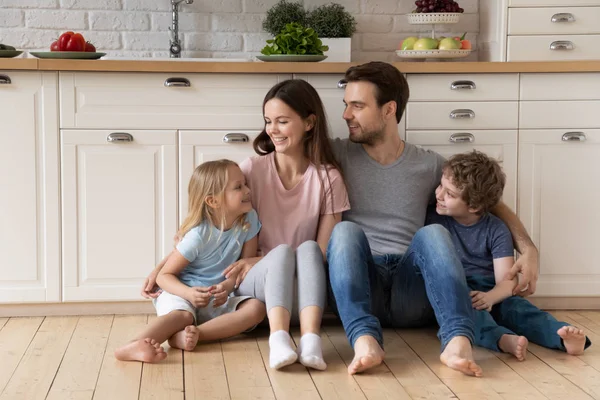 Happy tusenåriga far mor och små barn sitter på golvet. — Stockfoto