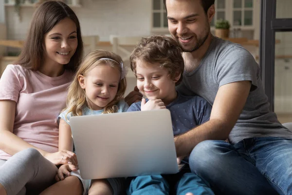 Glückliche junge Eltern, die mit niedlichen kleinen Kindern am Computer sitzen. — Stockfoto