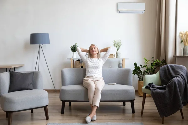 Relaxado mulher mais velha sentado no sofá na sala de ar condicionado — Fotografia de Stock