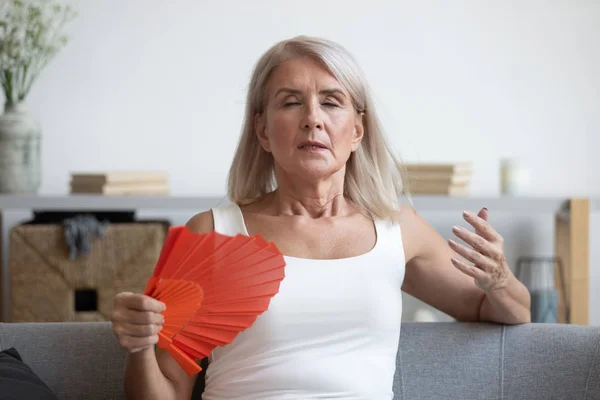 Müde reife Frau leidet unter Hitze zu Hause, winkt Ventilator — Stockfoto