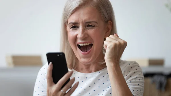 Tutup bersemangat wanita tua berteriak, menggunakan telepon, merayakan keberhasilan — Stok Foto