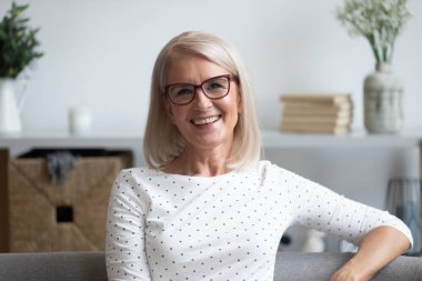 Head shot portrait smiling mature woman in glasses at home