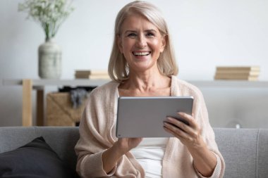 Happy mature woman using computer tablet, laughing at funny joke