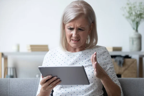 Раздраженная зрелая женщина, имеющая проблемы с компьютером планшет — стоковое фото