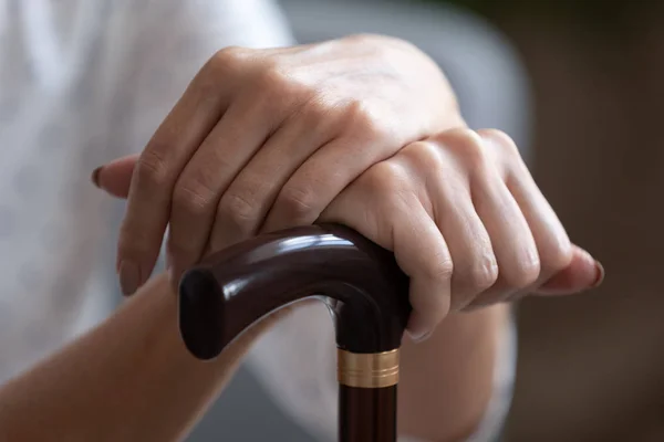 Oudere vrouw houdt handen op houten wandelstok close-up — Stockfoto