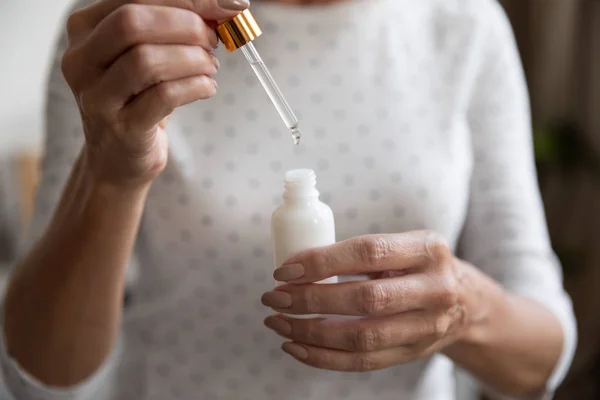 Close up mature woman dropping collagen moisturizer face serum — Stock Photo, Image