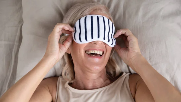 Selamat tersenyum wanita dewasa mengenakan topeng tidur berbaring di tempat tidur — Stok Foto