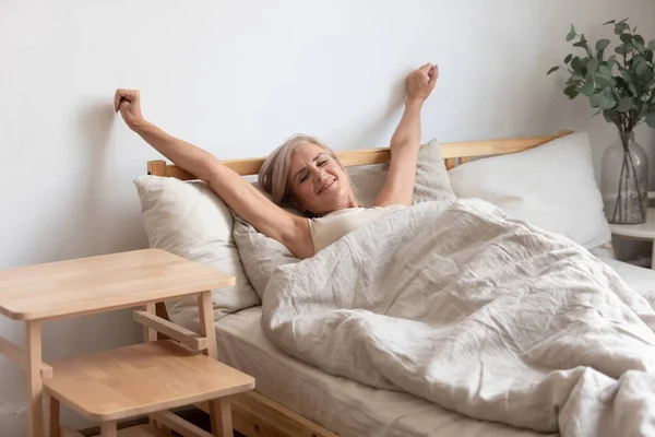 Wanita dewasa yang cantik meregangkan tangan di tempat tidur setelah terbangun — Stok Foto