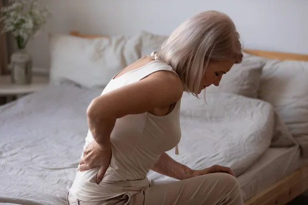 Mulher madura perturbada que sofre de dor nas costas, esfregando músculos rígidos — Fotografia de Stock