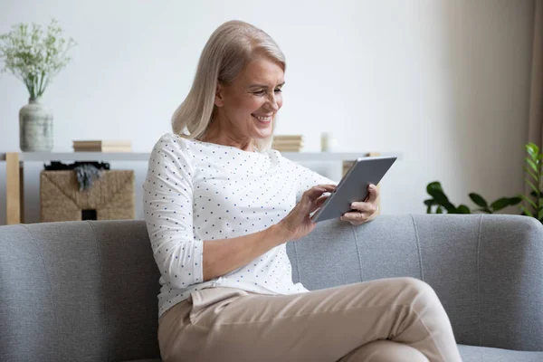 Mujer madura sonriente usando tableta de computadora en casa —  Fotos de Stock