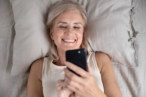 Selamat tersenyum wanita dewasa bersenang-senang dengan tampilan atas ponsel — Stok Foto