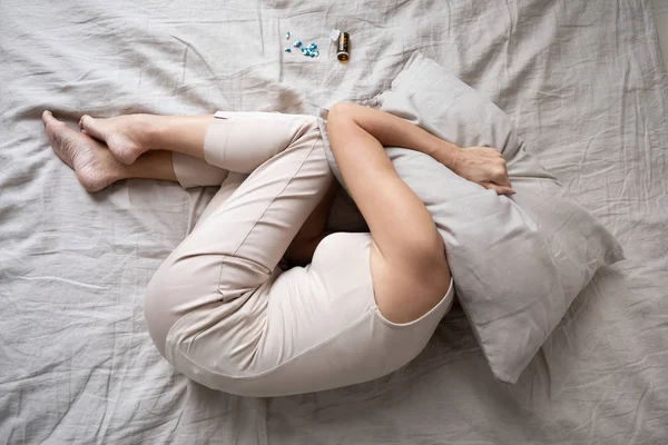 Wanita dewasa yang tertekan berbaring di tempat tidur dengan sebotol pil — Stok Foto