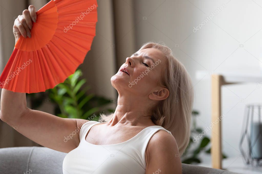 Exhausted older woman waving fan close up, suffering from heat
