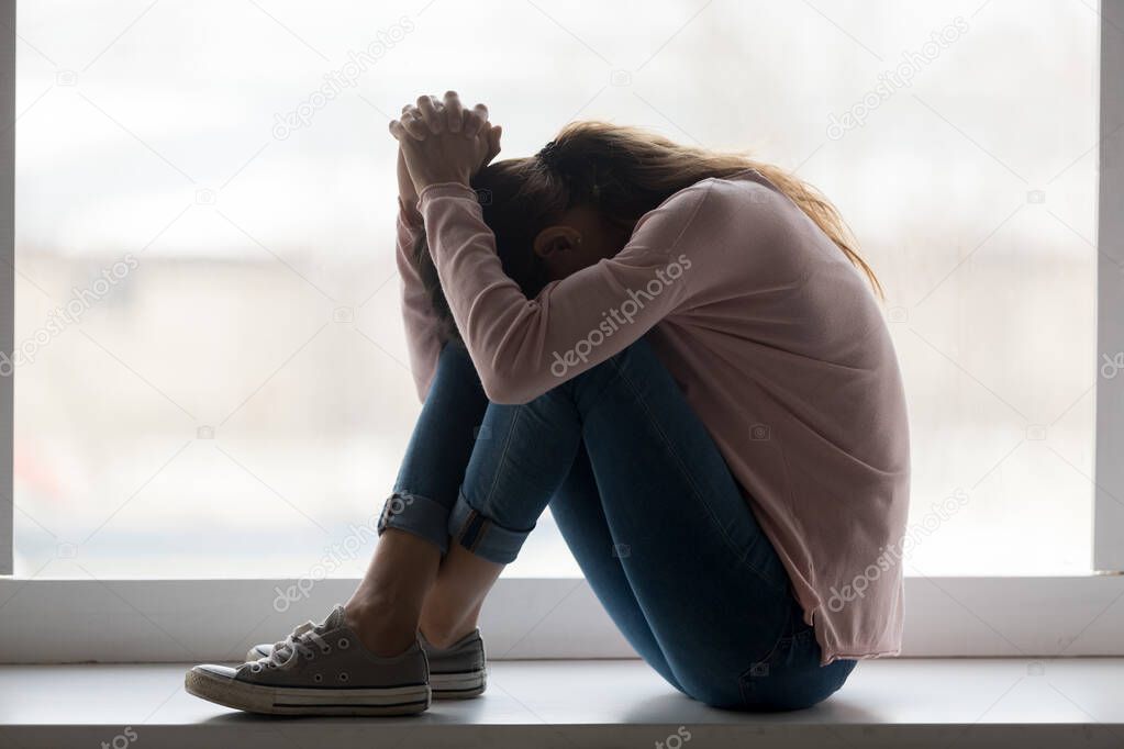 Depressed sad teen girl sit on sill crying at home