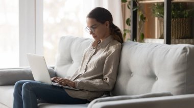 Ciddi genç bayan evde dizüstü bilgisayarda çalışıyor.