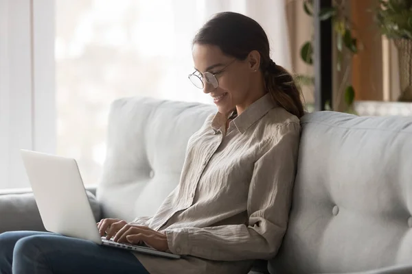 Mujer joven sonriente usando el ordenador portátil sentarse en el sofá en casa — Foto de Stock