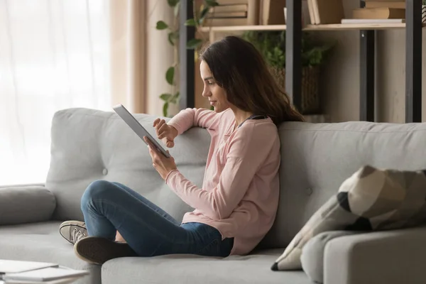 Mladá žena s digitálním tabletem sedí doma na pohovce — Stock fotografie