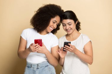 Gülümseyen bin yıllık çoklu etnik kız arkadaşlar cep telefonlarıyla gülerler.