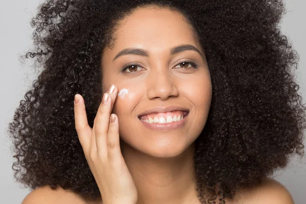 Sonriente chica biracial aplicar crema facial hidratante — Foto de Stock