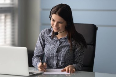 Gülümseyen iş kadını eğitici web sitesini izliyor, notlar yazıyor..